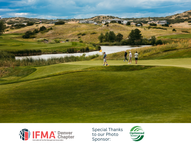 Golfers on a green near water, surrounded by rolling hills under a cloudy sky.