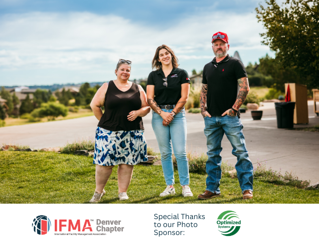 Three people stand on a grassy area outdoors. Woman in skirt, woman in jeans, and man with tattoos pose for photo.