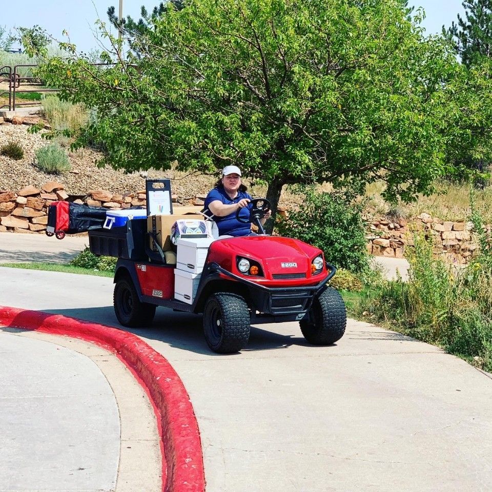 Person driving a red and white golf cart on a path at a golf course.