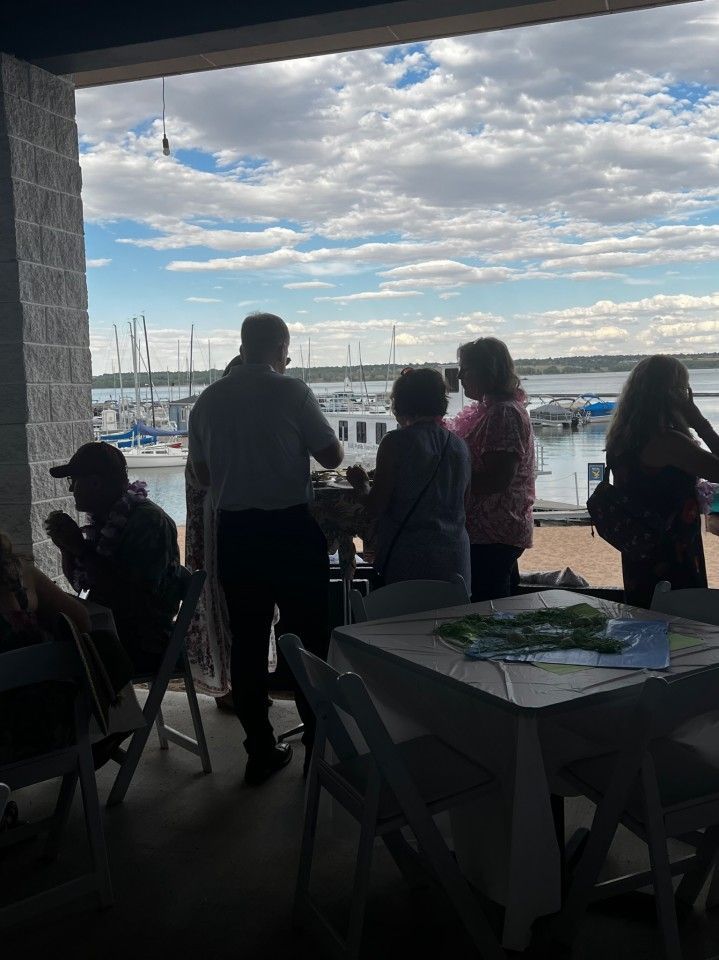 People standing on a patio, looking out at a harbor with boats on a cloudy day.