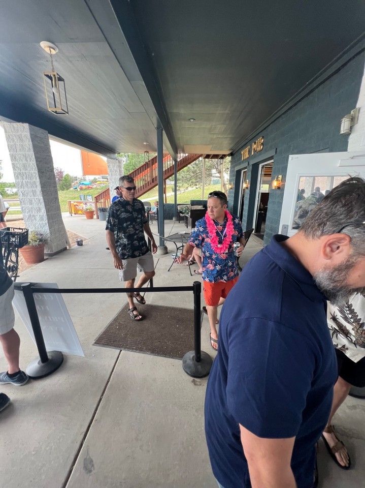 People in line outside a building, one wearing a floral lei.