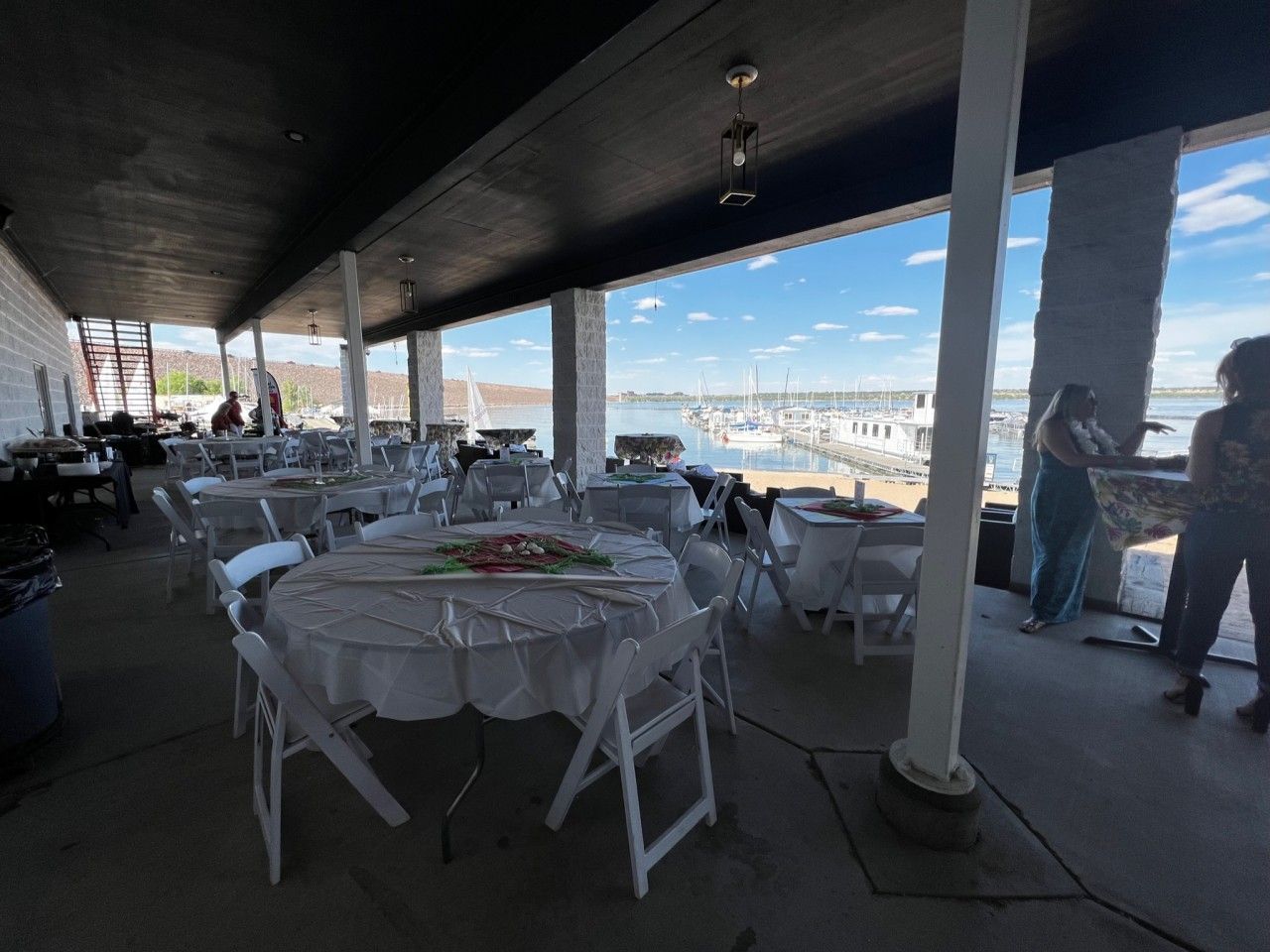 Outdoor event venue with tables set for a gathering, waterfront view in the background.