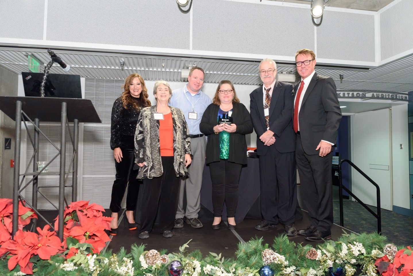 People on a stage with an award, festive decorations.