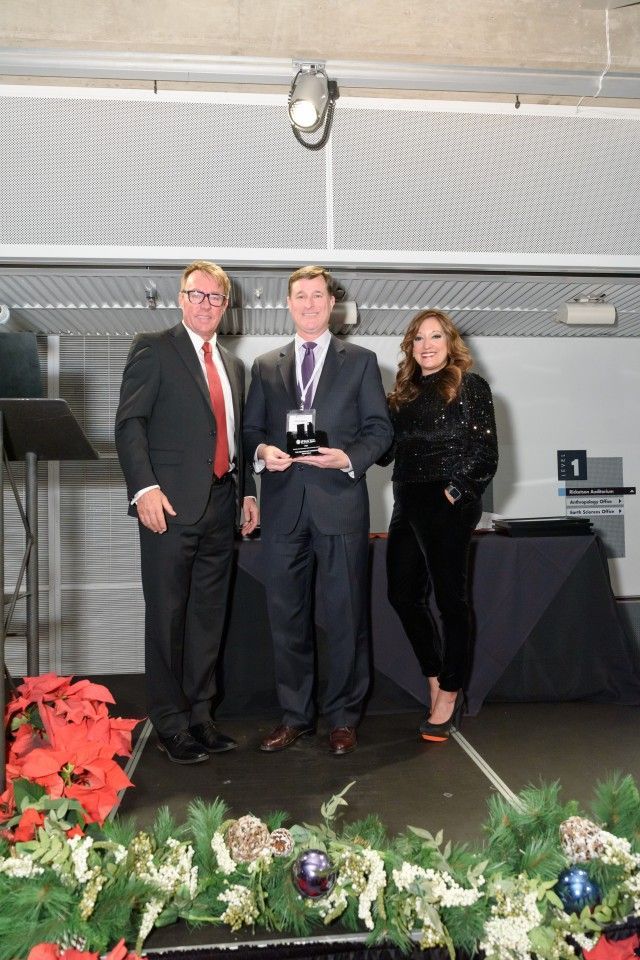 Three people on stage, one holding an award, with holiday decorations.