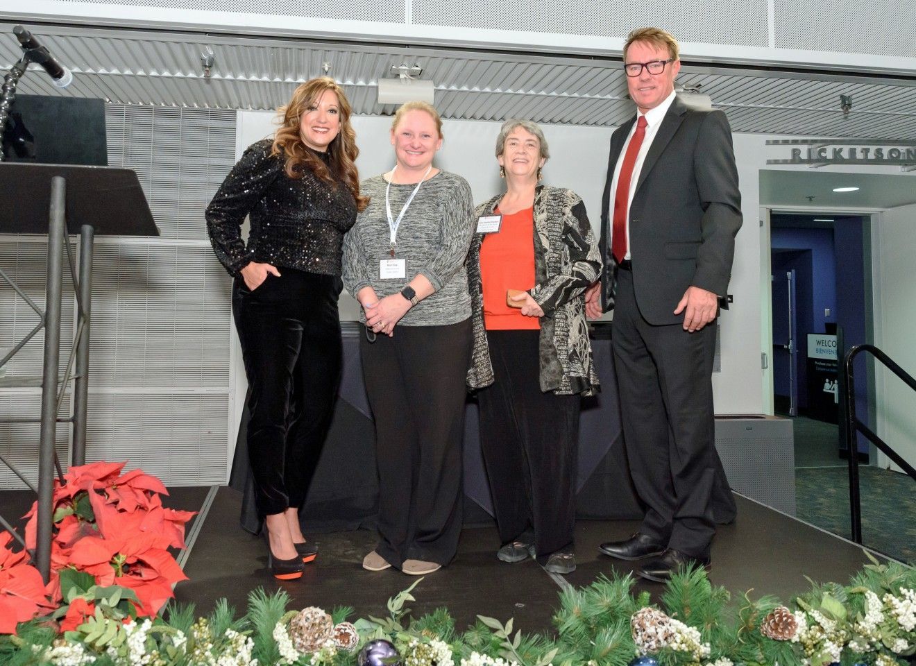 Four people posing on a stage with festive decorations.