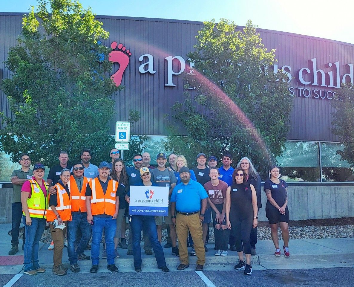 Group of people holding a sign, standing in front of a building with “a precious child” on it.