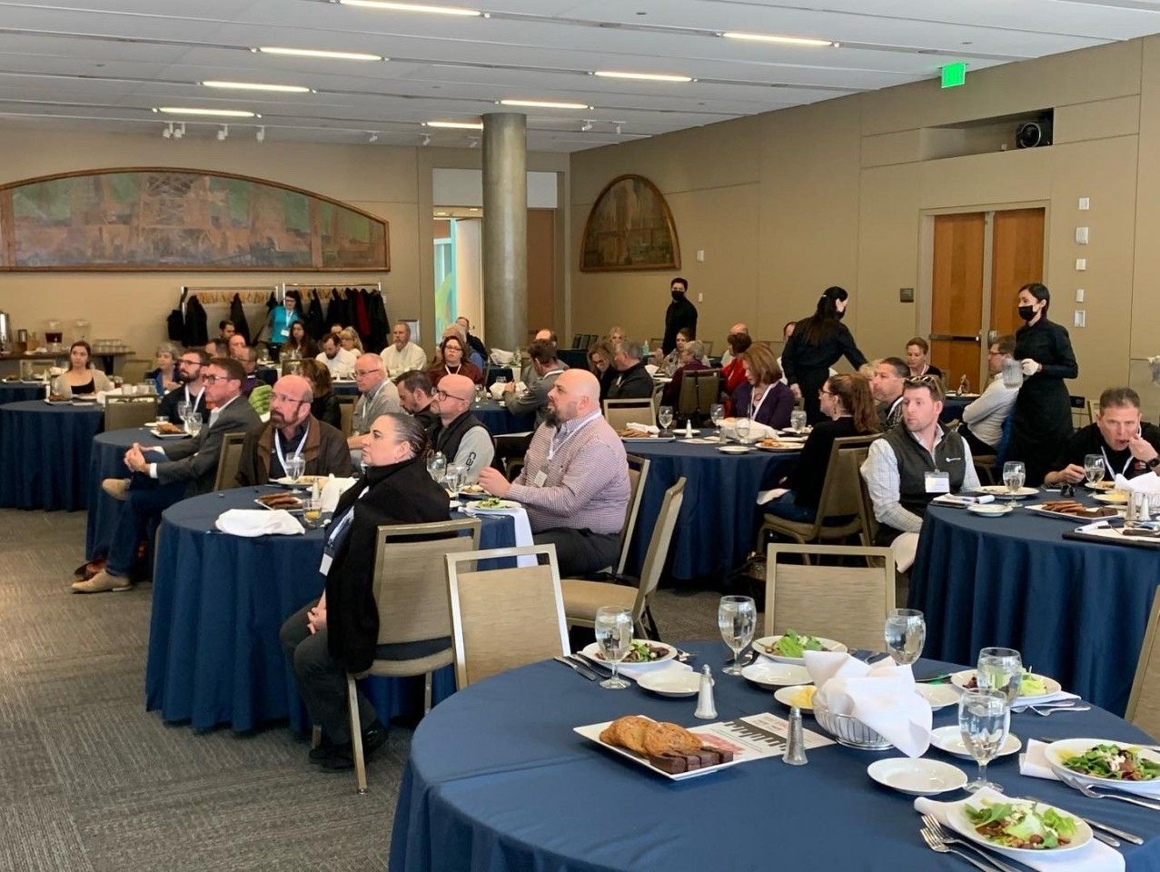 People seated at round tables in a conference room, attending an event. 
