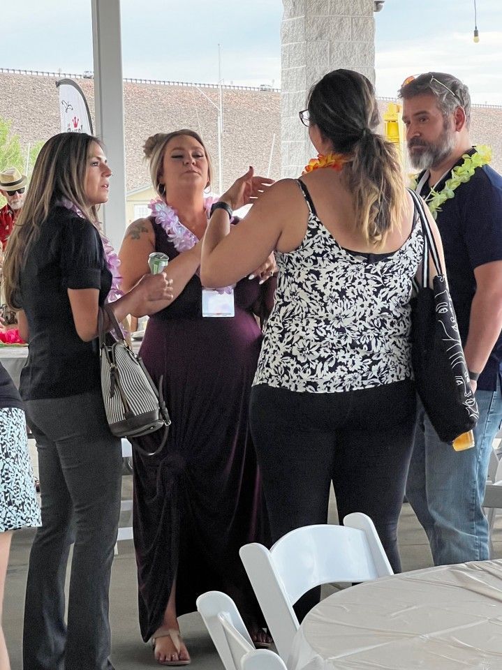 Four people, two women wearing leis, conversing at an outdoor event.