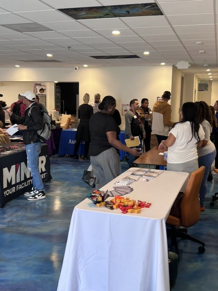 People at tables in a room, some looking at displays. Blue-tinted floor.