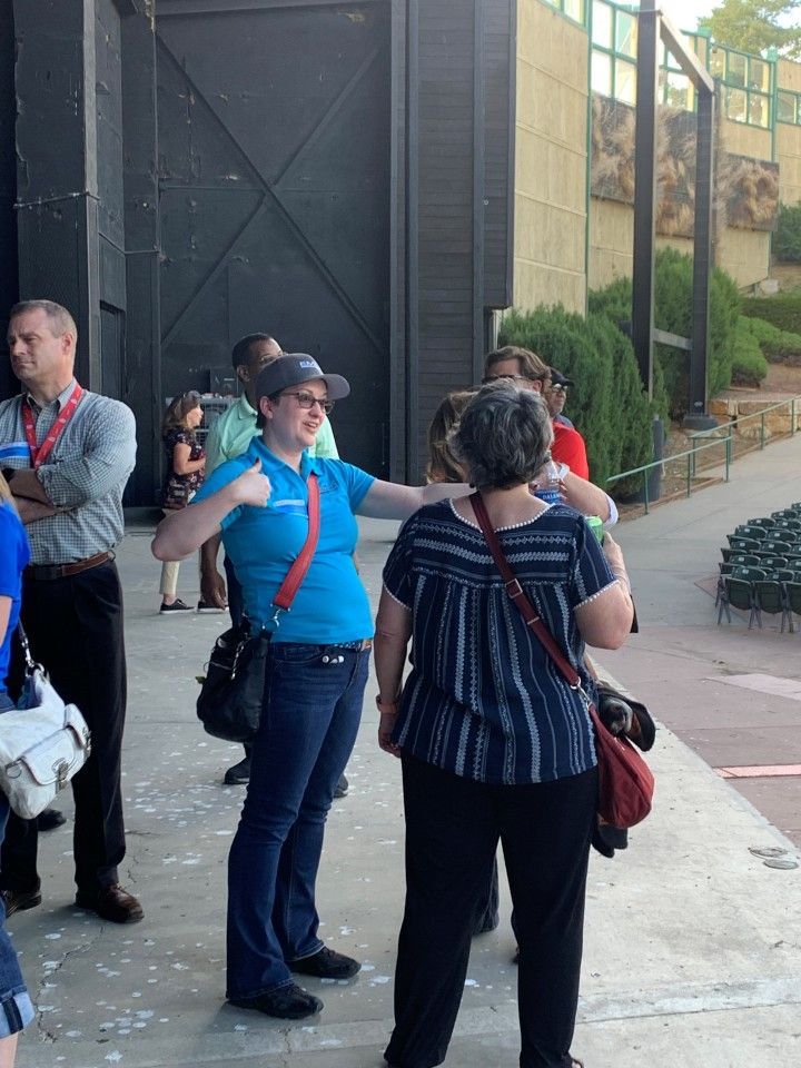 A group of people standing outside a building. One woman in blue gestures enthusiastically.