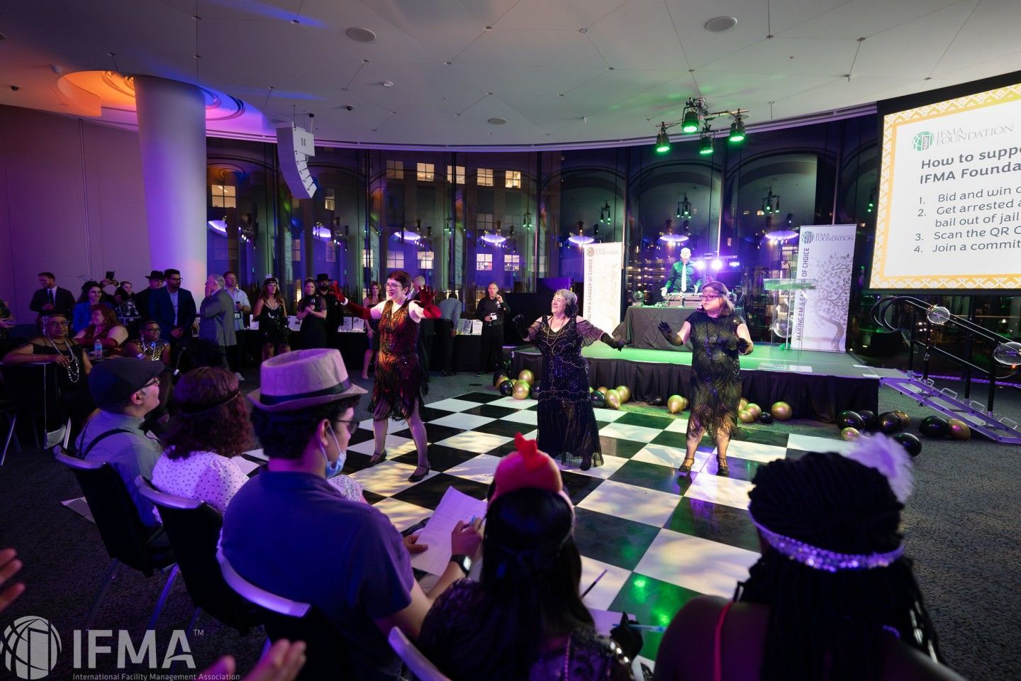 Event with performers on a checkered dance floor, stage with band, audience watching.