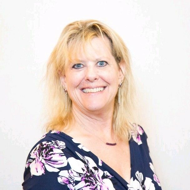 Woman with blonde hair smiling, wearing a floral navy top, against a white background.