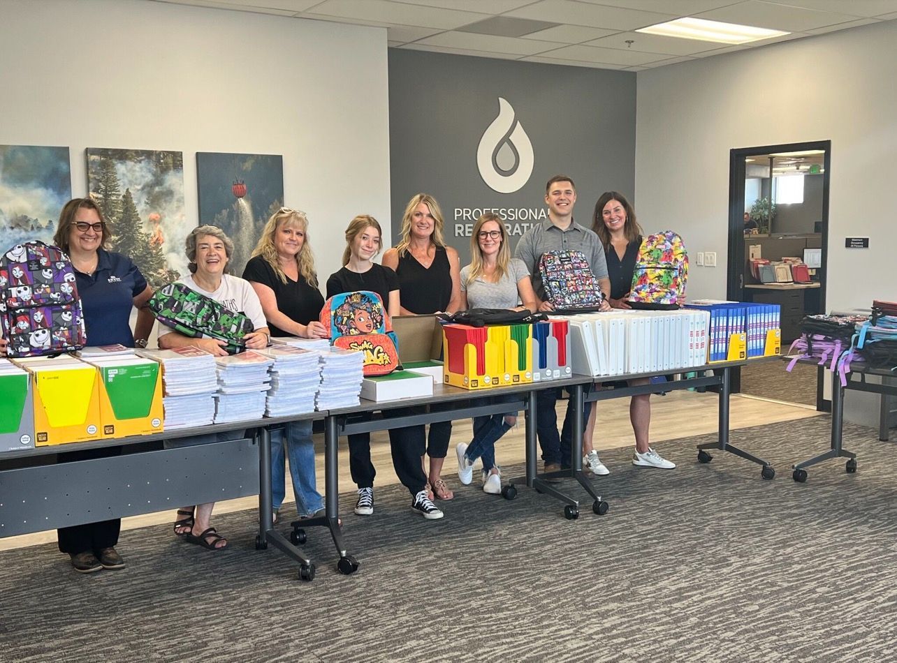 Group of people standing behind tables laden with school supplies in an office.