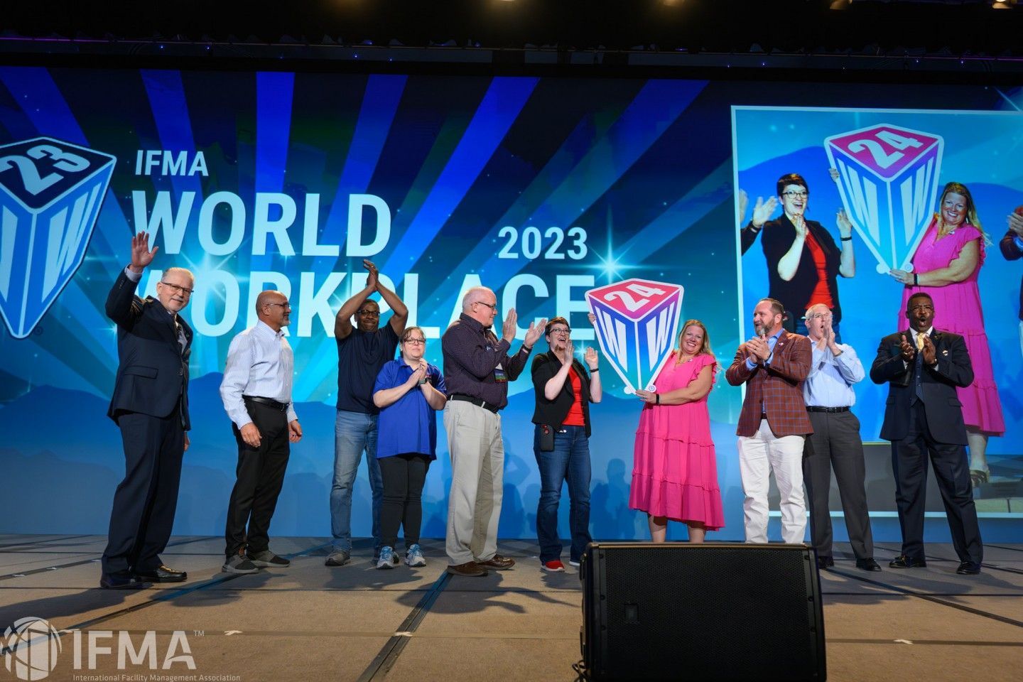 Group of people on stage at an event, World Workplace 2023, with large logo. They're applauding and smiling.