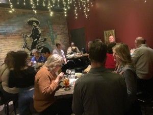 People seated at tables in a dimly lit restaurant, some eating, with a mural and decorative lights.