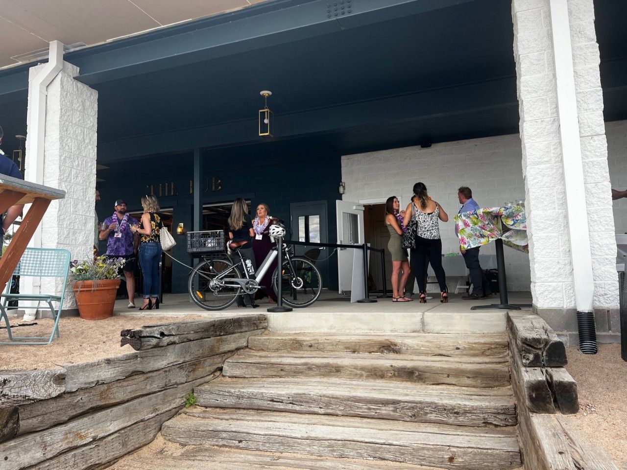 People gathered on a porch with steps, a bike, and a stage. Blue and white building.