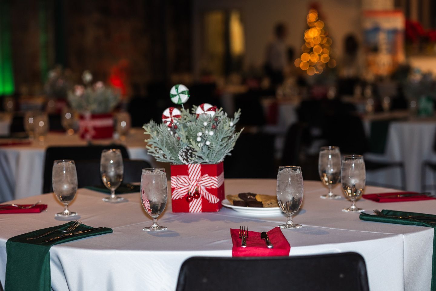 Round table set for a holiday event with red and green decor, centerpieces, and glasses of water.