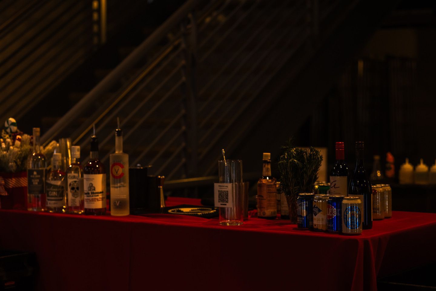 A red table with bottles of liquor and wine set up outdoors at night.