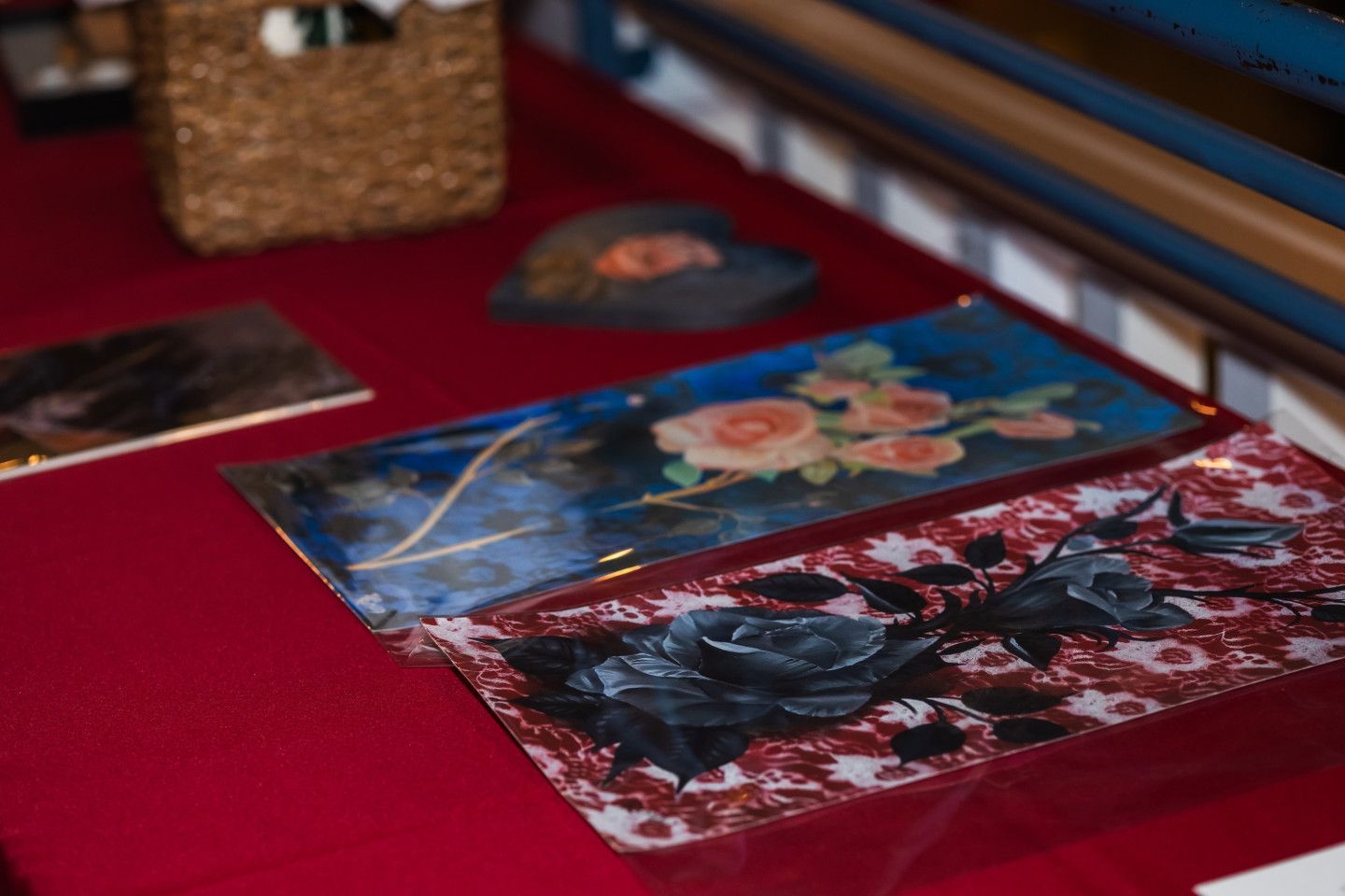 Three decorative glass panels with floral designs sit on a red surface, with a woven basket visible in the background.