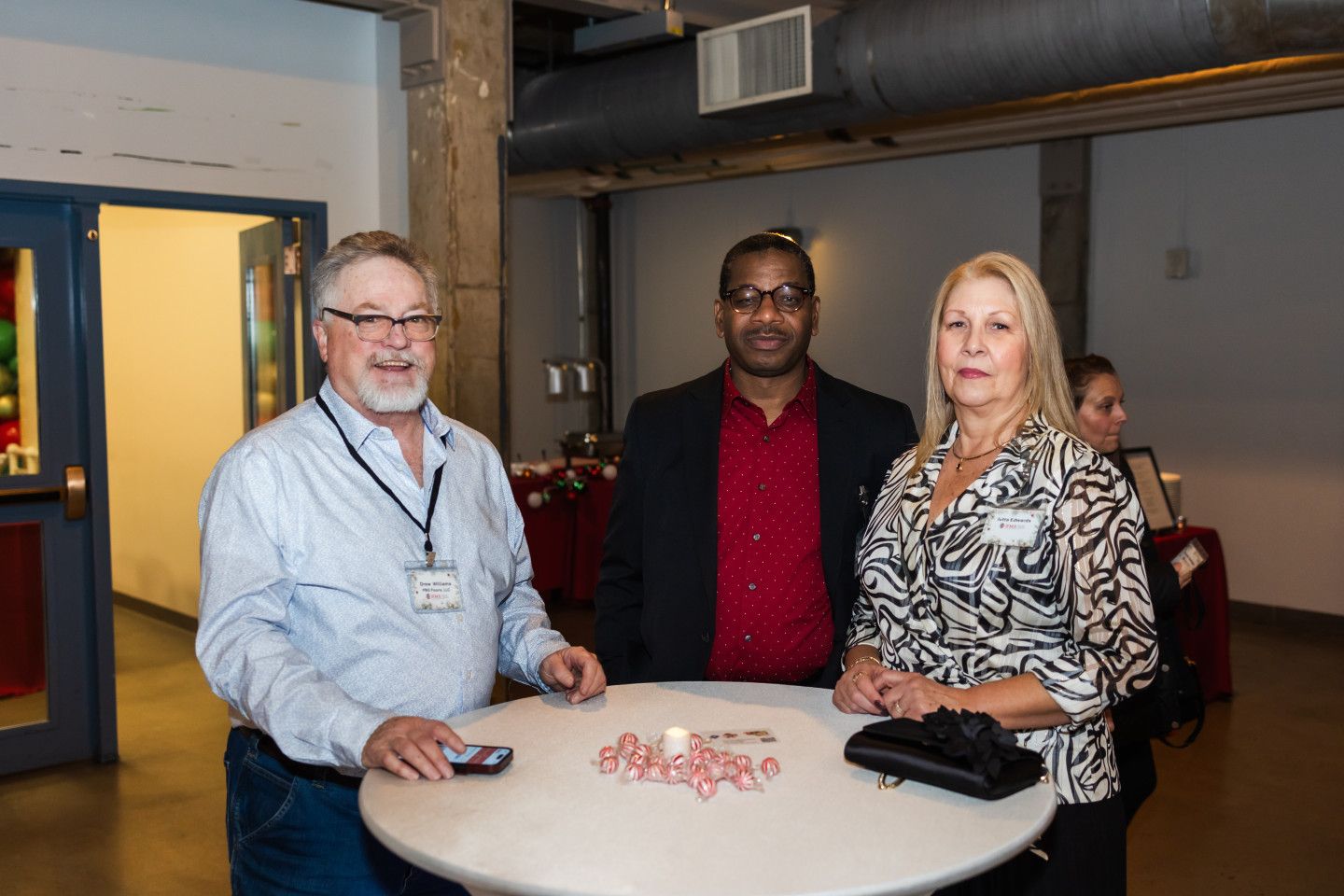 Three people at a reception stand around a small table with pink candies.
