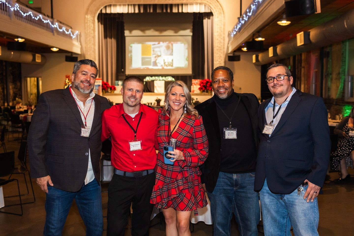 Five people posing together at an event with a stage in the background.