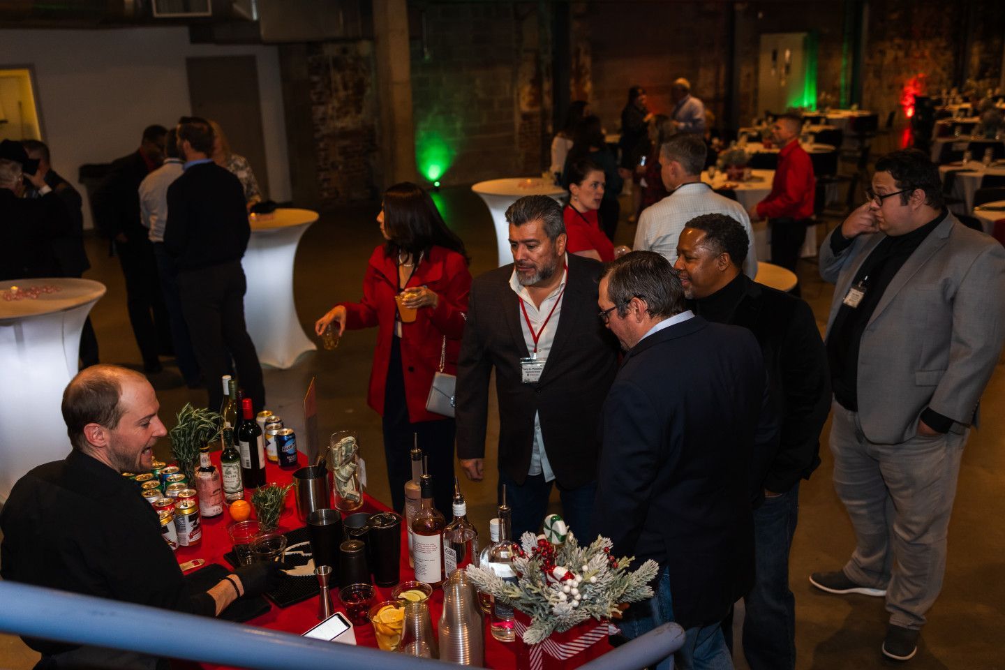 People mingling at an event with a bar. White high-top tables, decorative lights, and drinks on display.