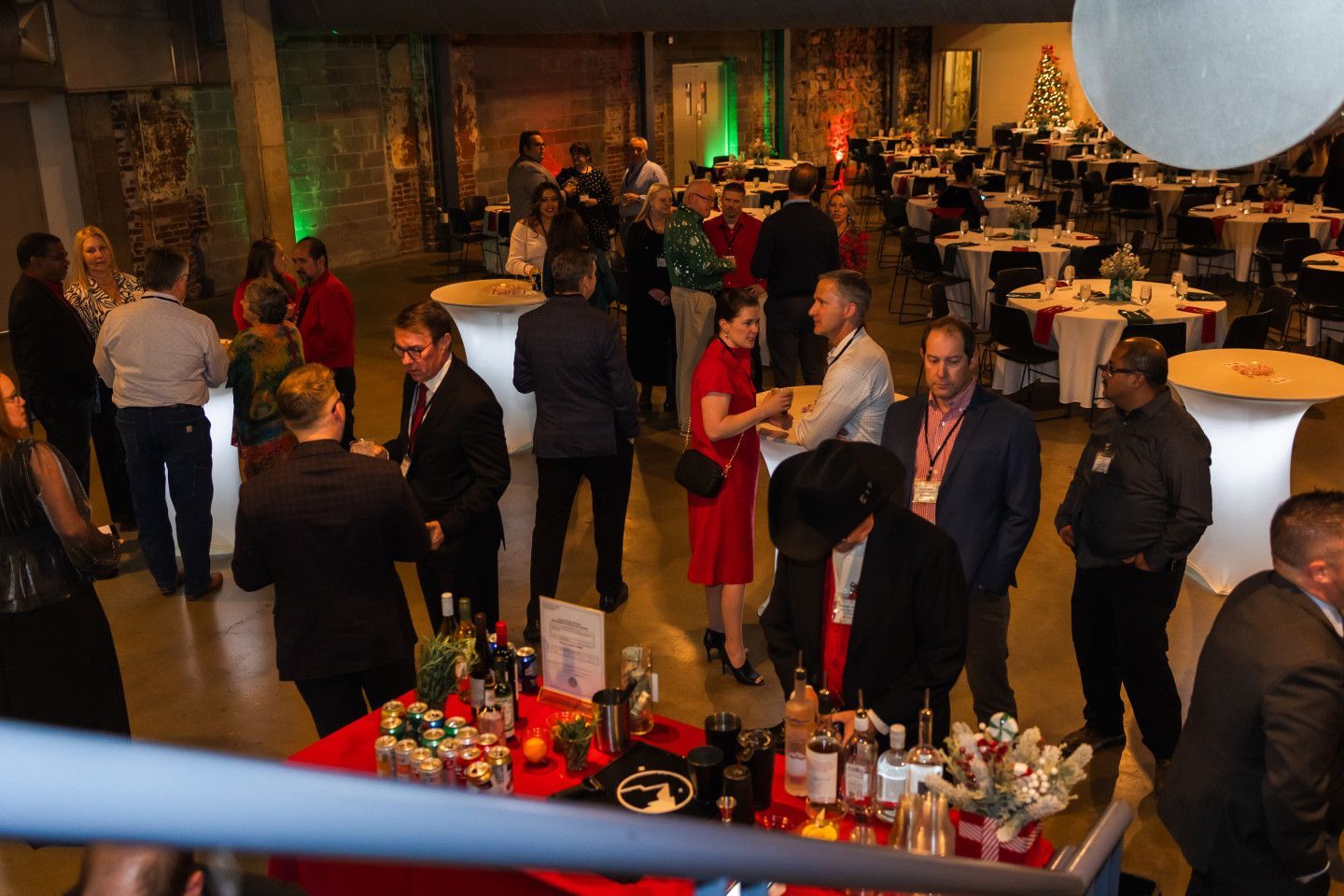 People at an event mingle in a room with a bar, tables, and decorations.