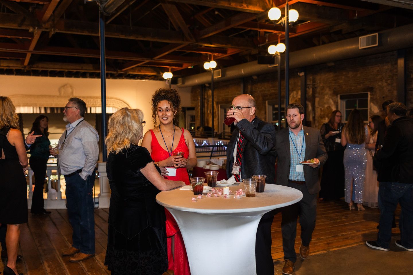 People socializing at an event with drinks in a room with industrial design elements.