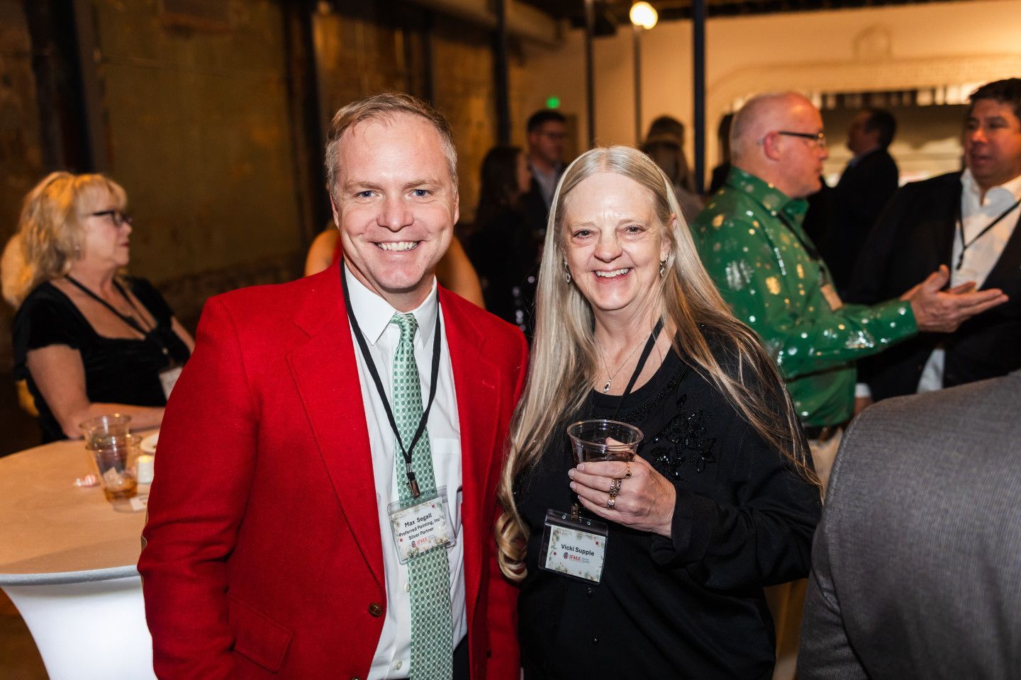 Man in red blazer and woman in black top smile at a social event.