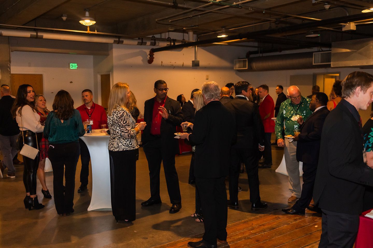 People socializing at an event with food and drinks. Some are wearing red and black, in a brightly lit room.