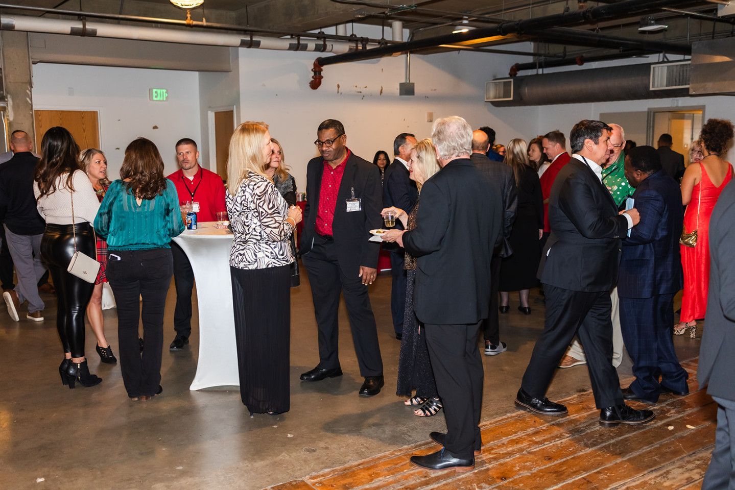 People mingle at an event with a white cocktail table in a modern industrial-style space.