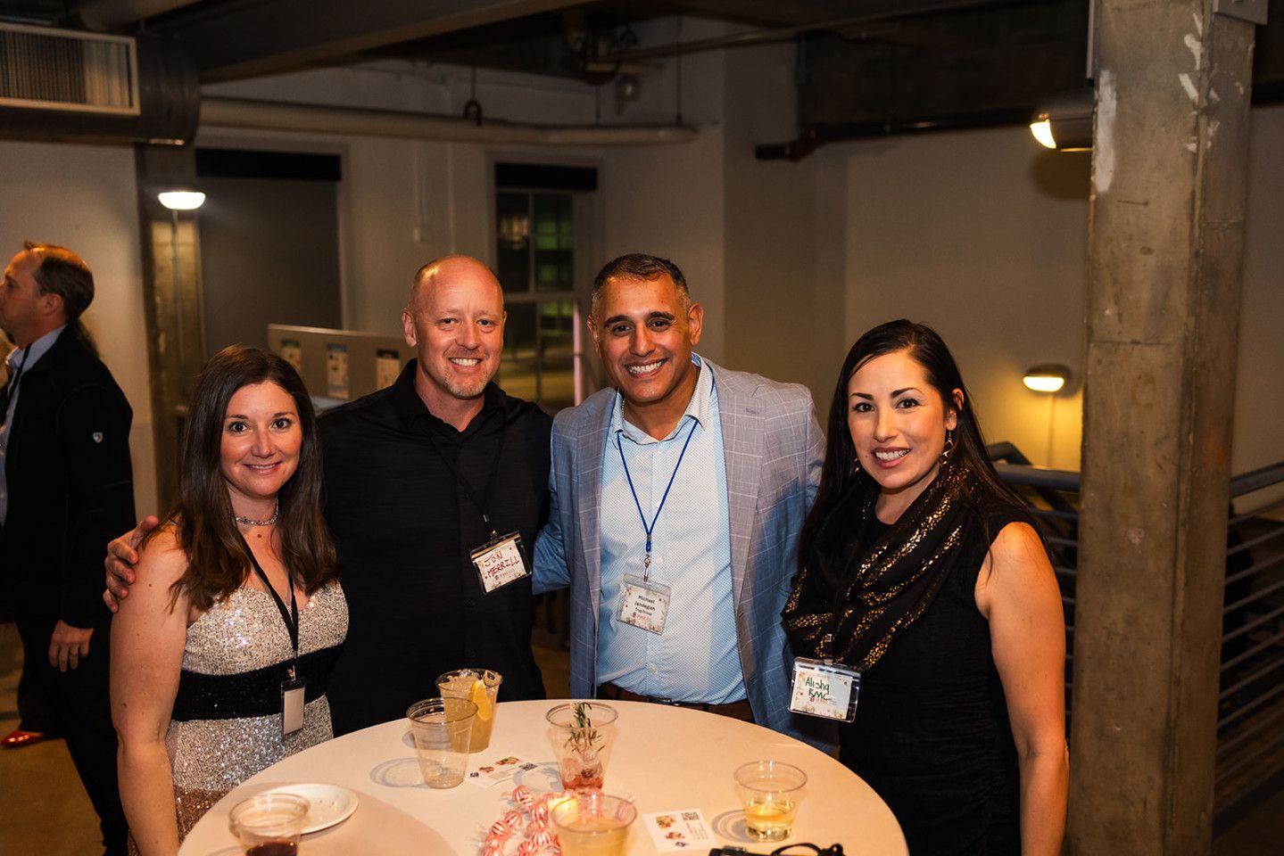 Four people smiling together at an event, gathered around a small table with drinks.