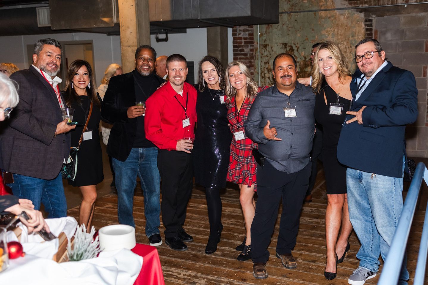 Group of people at an event, smiling. Men in jackets, several women in dresses, indoors.
