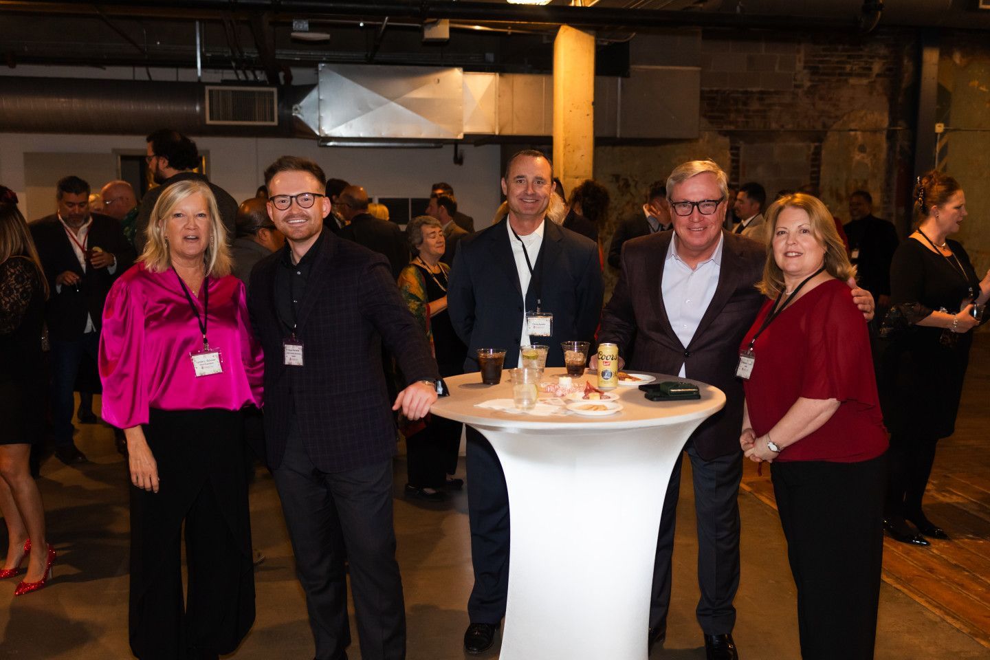 Group of five people at an event, standing around a small table, in an industrial-style room.