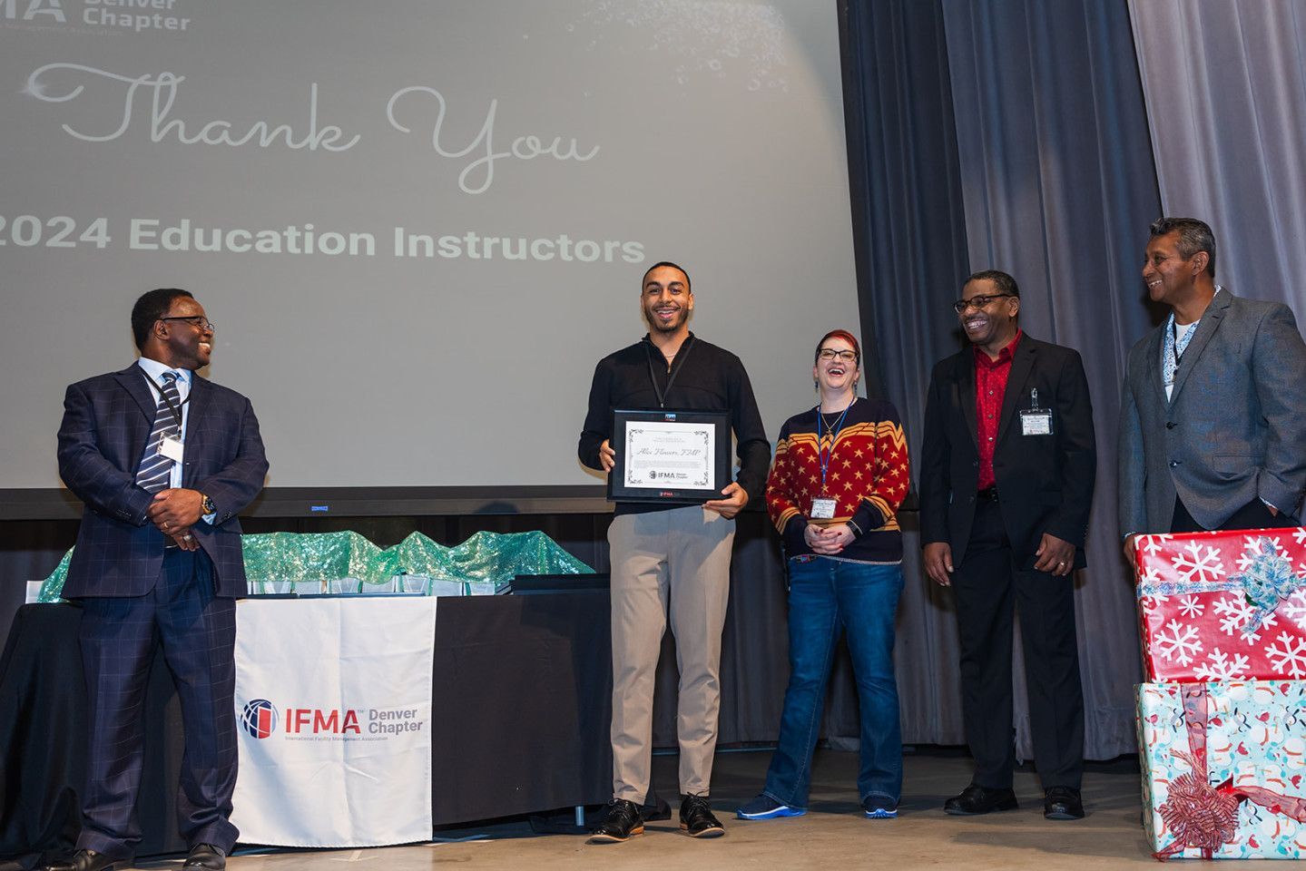 Man accepts award on stage; others look on. Thank you banner visible. IFMA logo.