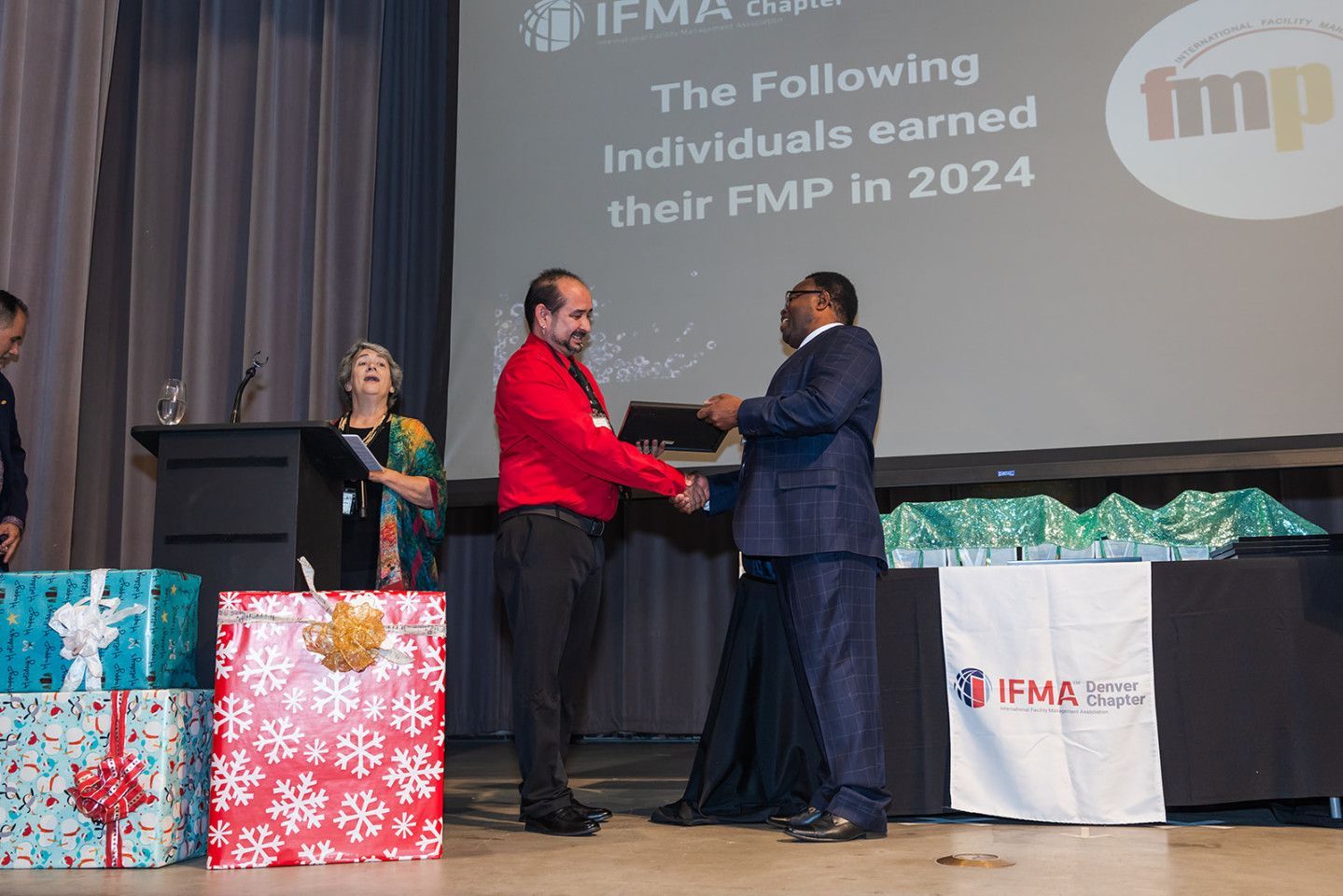 Man in red shirt receiving an award from a man in a suit on a stage.