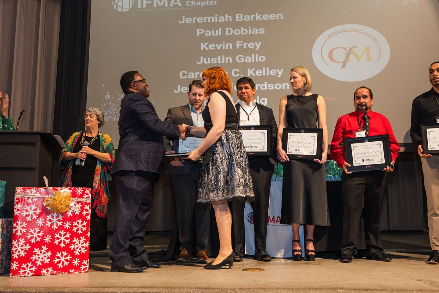 Man presenting an award to a woman on a stage. Other people stand with certificates.