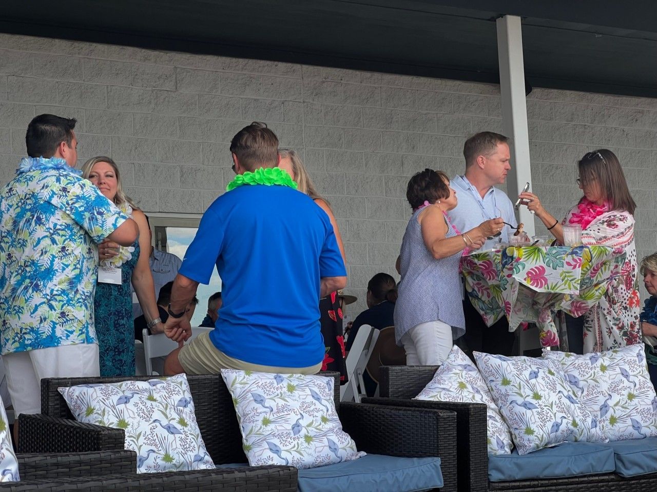 People in Hawaiian shirts at an outdoor event, exchanging gifts, sitting on patio furniture.