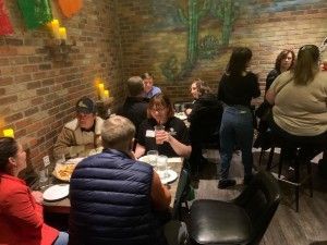 Restaurant interior with people at tables. Some are eating, others are talking and some are at the bar.