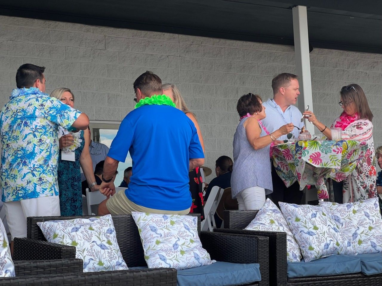 People at a party, some wearing floral shirts and leis, near outdoor seating.