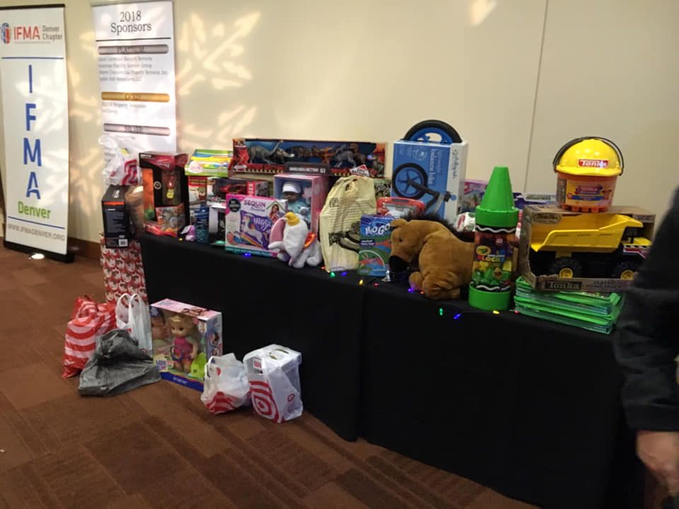 Table with toys: dump truck, bear, doll, gifts, backdrop with logos, Denver.