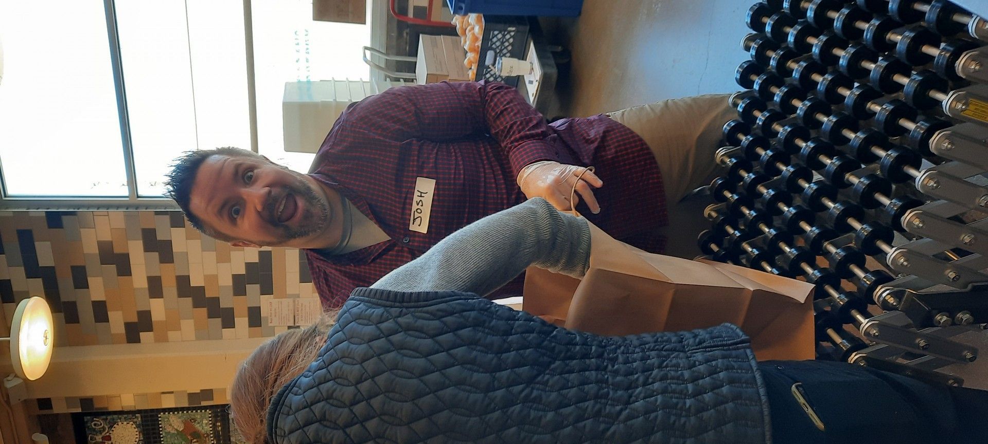 Man smiling, leaning over. Arm in a cast, cardboard box. Wine bottle storage in the background.
