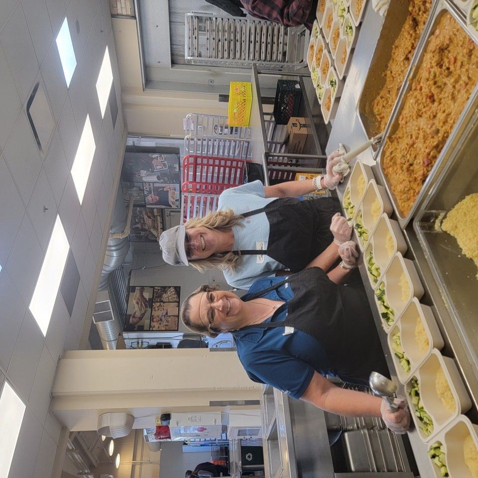Two people in aprons filling food containers in a commercial kitchen.