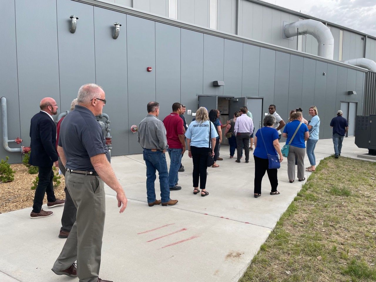 Group of people outside a gray building with an open door.