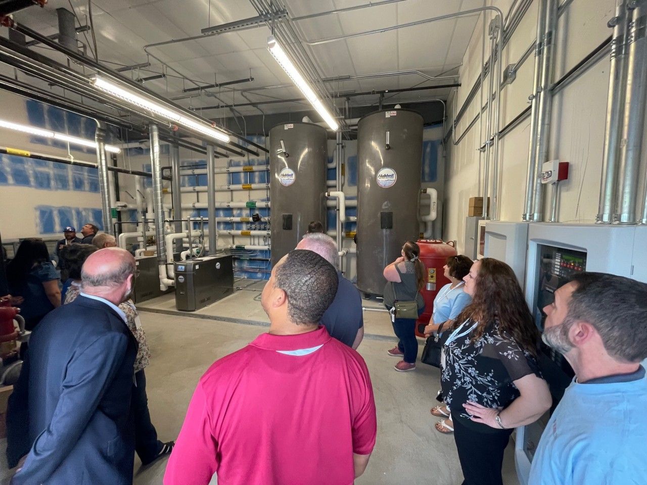 People tour an industrial facility, looking at tall cylindrical tanks and piping.
