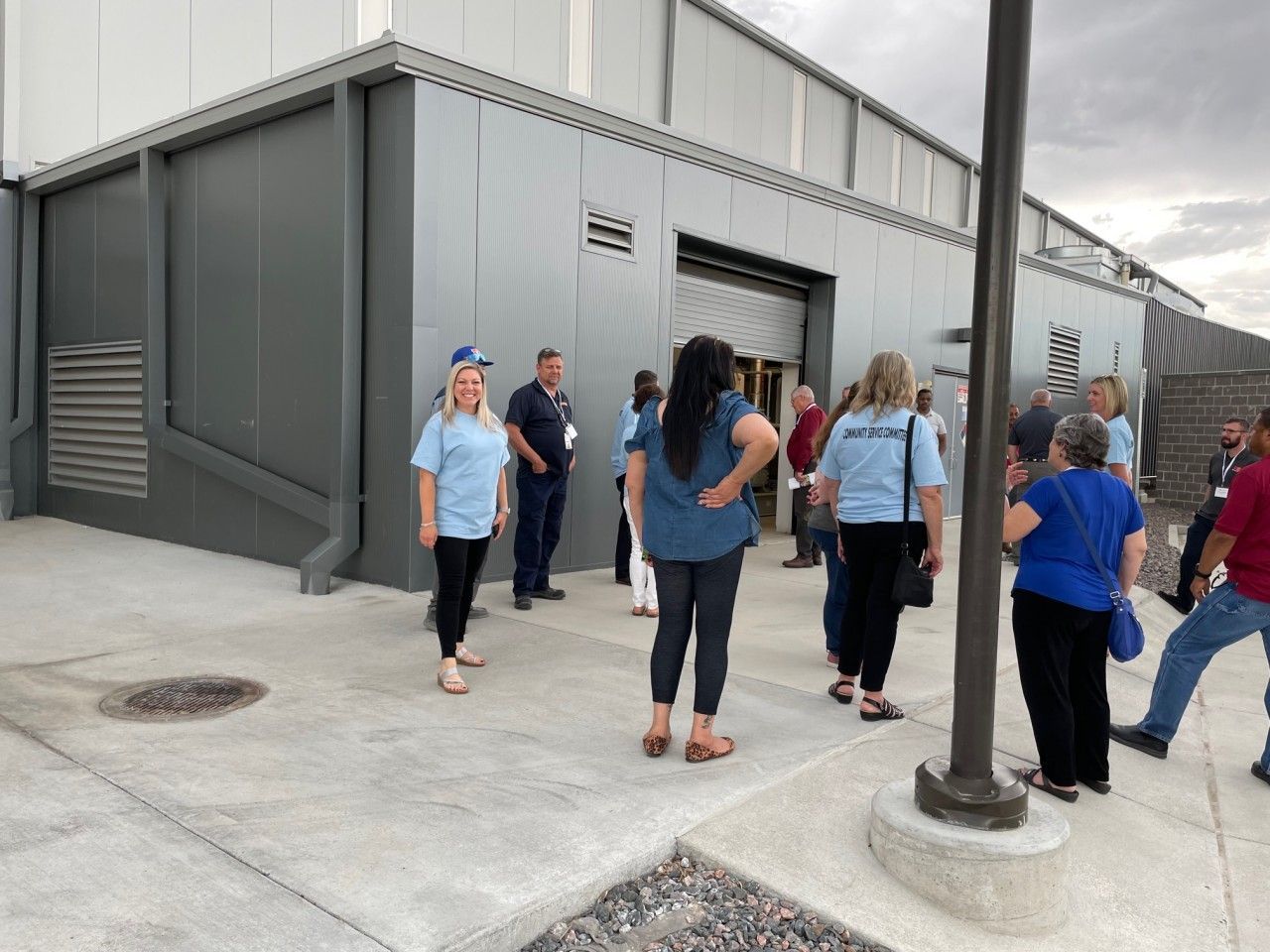 People outside a gray building with an open door. Several wear blue shirts.