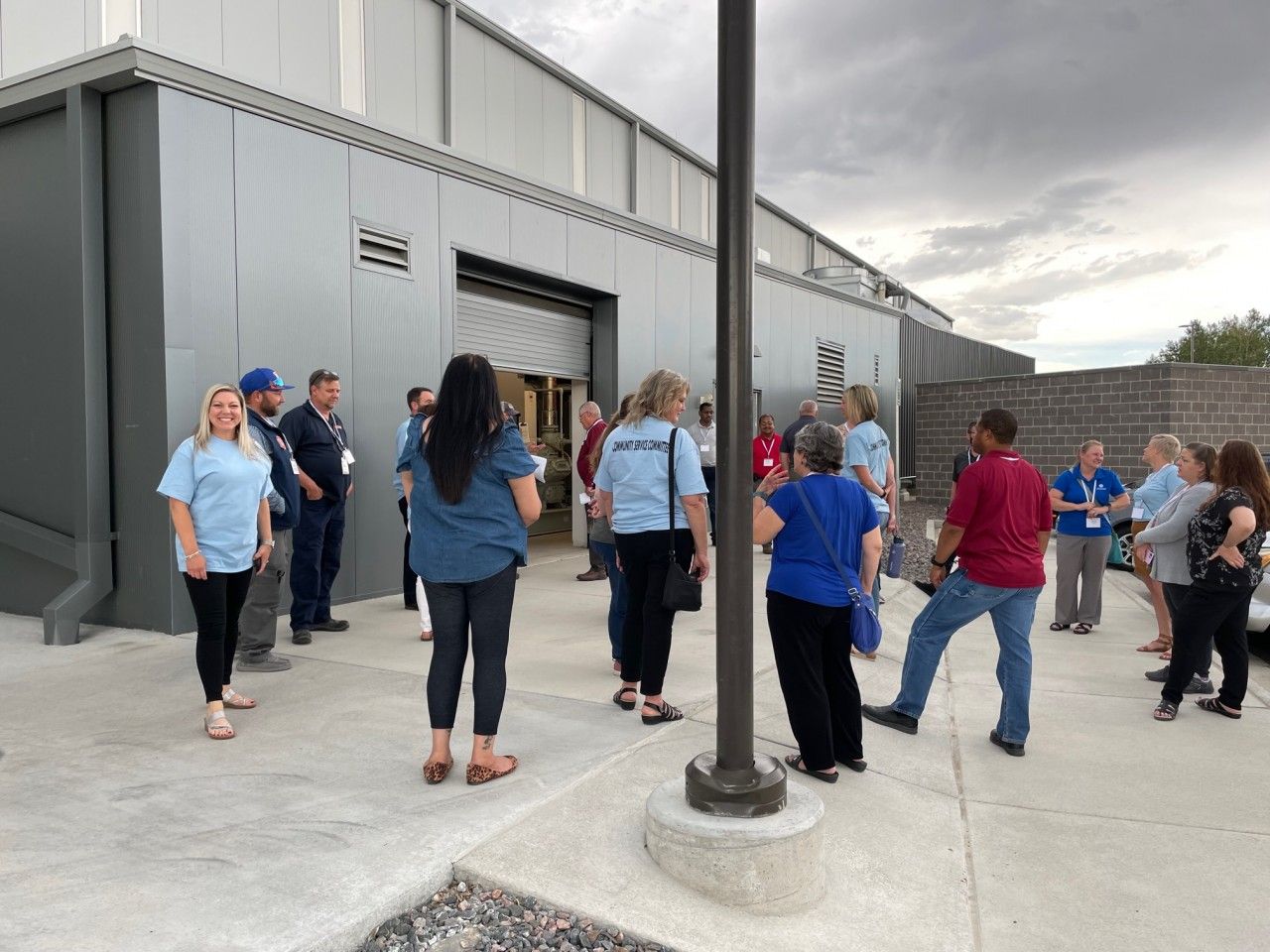 Group of people in light blue shirts standing outside a building with a large door.