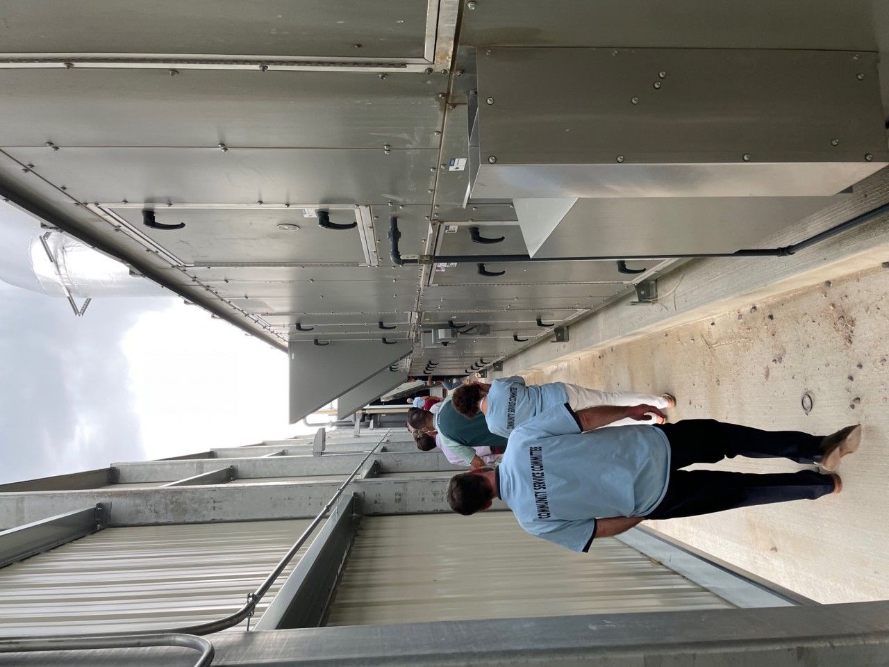 People in blue shirts walking below metal structures outdoors.