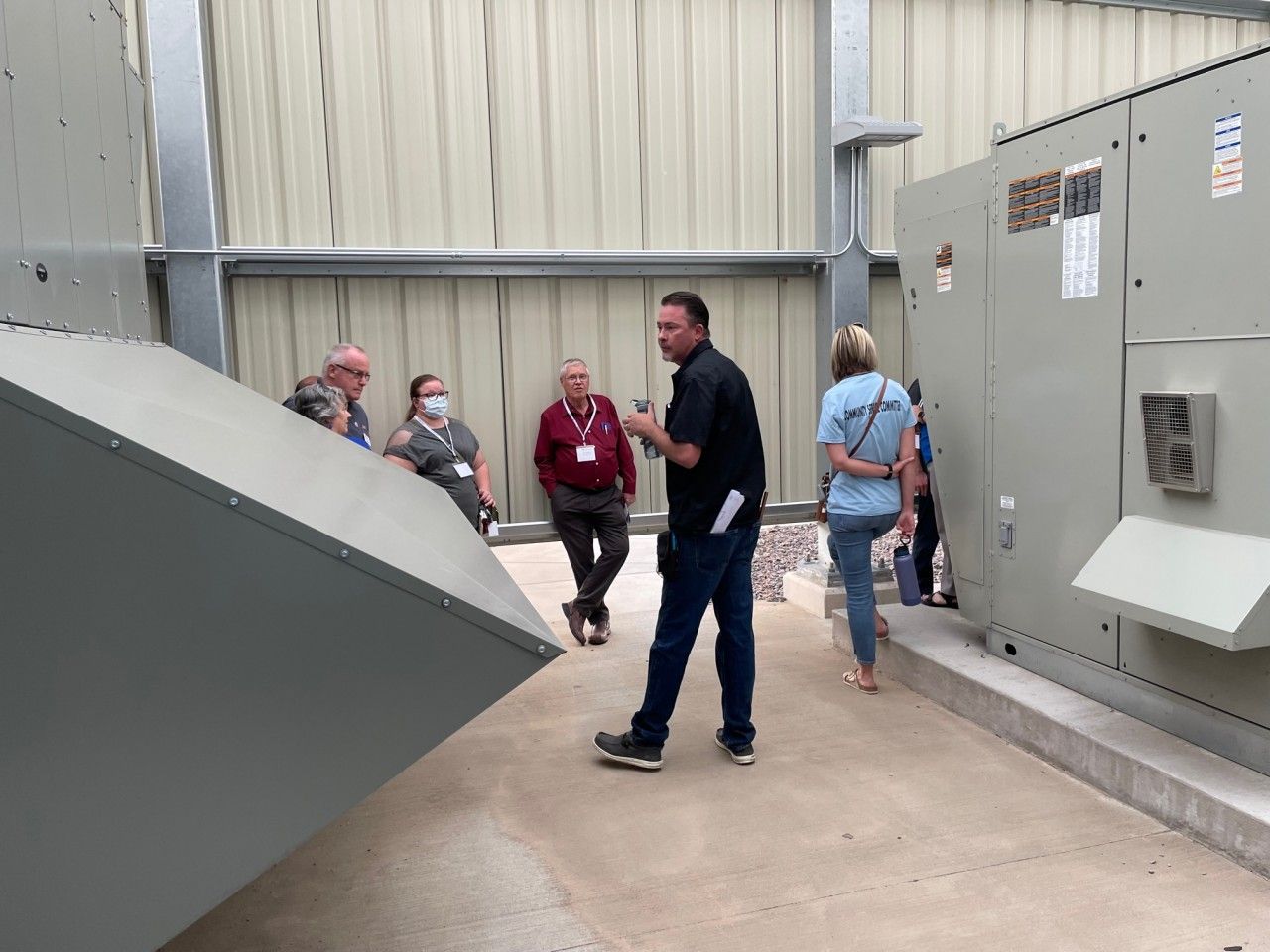 A man points toward HVAC equipment as a small group listens inside a building.