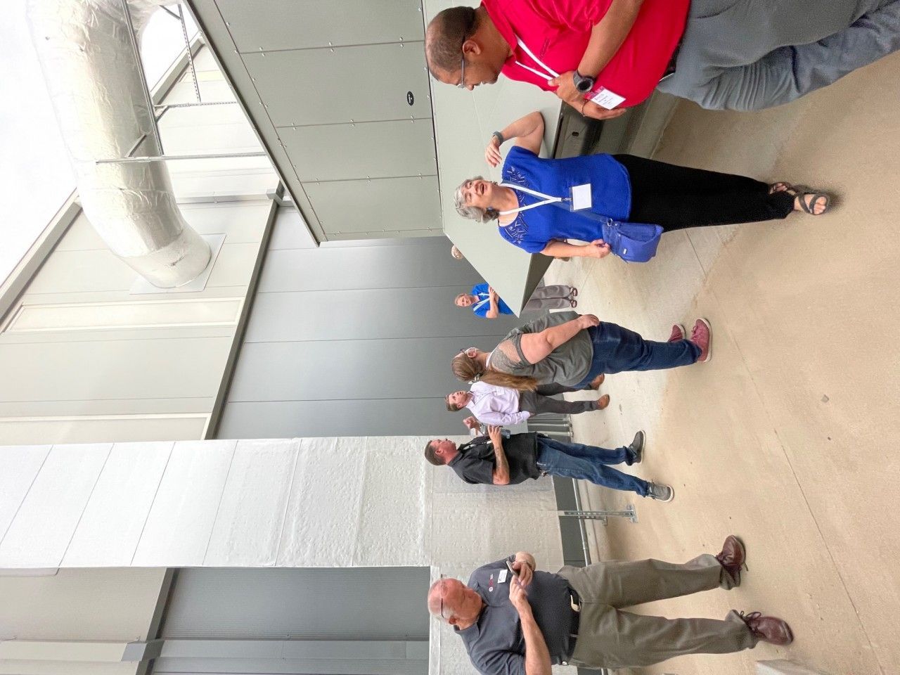 People observing equipment, standing near ductwork in an industrial setting.